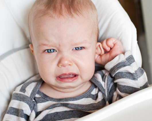 Unhappy infant tugging on ear, a possible sign of an ear infection
